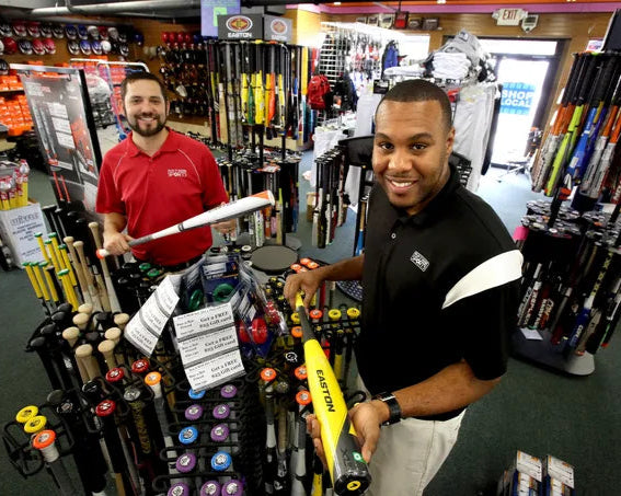 Two men in a sports equipment store holding baseball bats.